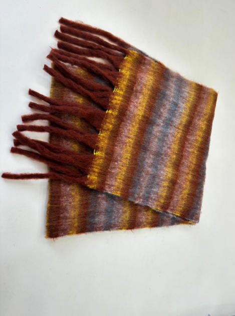 Folded fluffy striped scarf in rust, mustard yellow, and blue tones with long fringe ends on white background
