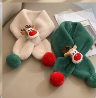 Two plush children's scarves with reindeer face appliqué and red pompom ends in cream and green colors on flat lay