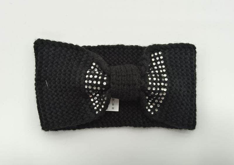 Black chunky knit winter headband with decorative rhinestone-studded bow detail, laid flat on white background