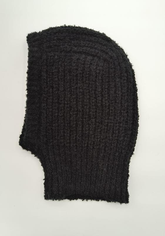 Black chunky ribbed knit balaclava laid flat on white background, bouclé textured wool full face mask with frayed edges