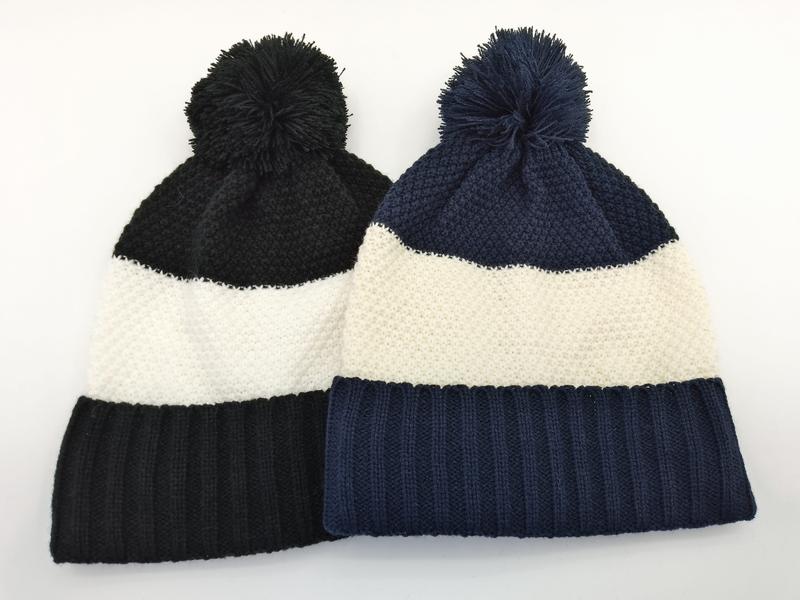 Two color block knit beanies with pom-poms in black-white and navy-white stripe patterns laid flat on white background