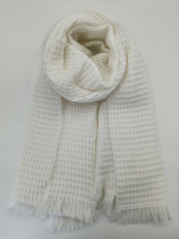 Ivory white waffle knit scarf with fringe ends, rolled and laid flat on white background showing textured grid pattern