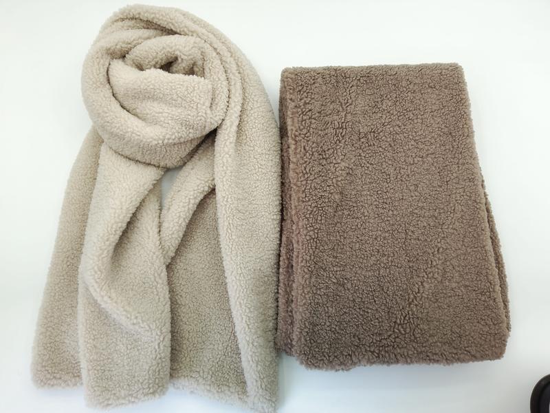 Two sherpa fleece scarves in beige and taupe colors, one draped and one folded flat, showing soft teddy bear texture