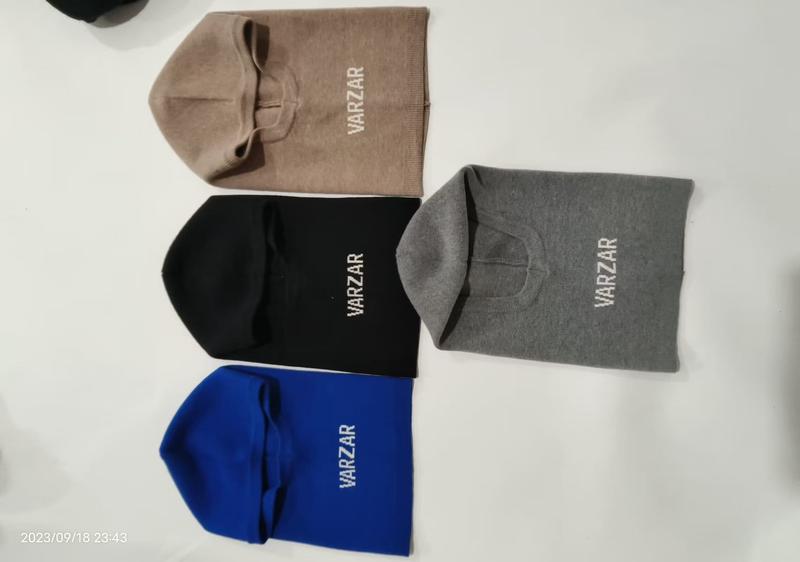 Four knit balaclava beanie hats in beige, black, gray, and blue laid flat on white surface with embroidered logo