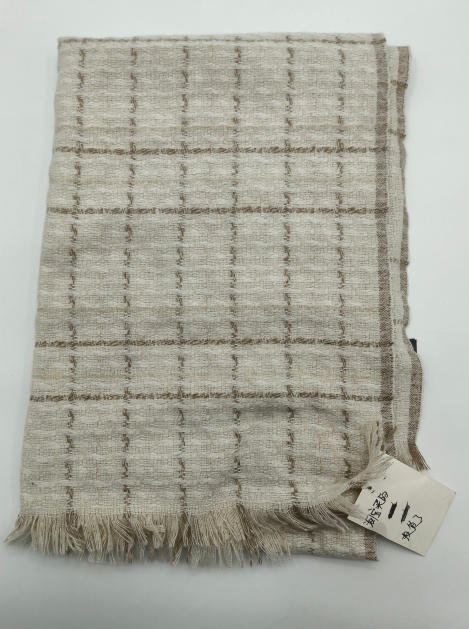 Folded ivory and beige woven plaid throw blanket with fringe trim and textured grid pattern