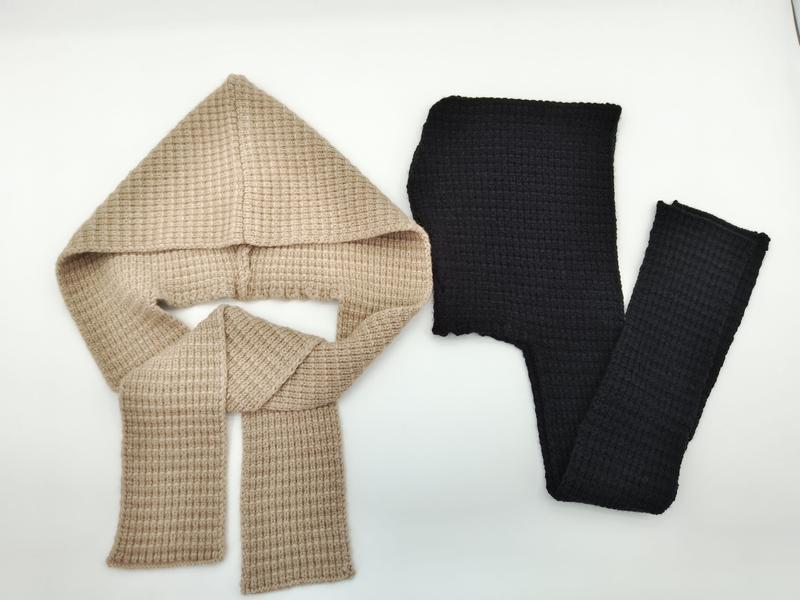 Two waffle knit hooded scarves laid flat, one beige with hood and scarf ends, one black, on white background