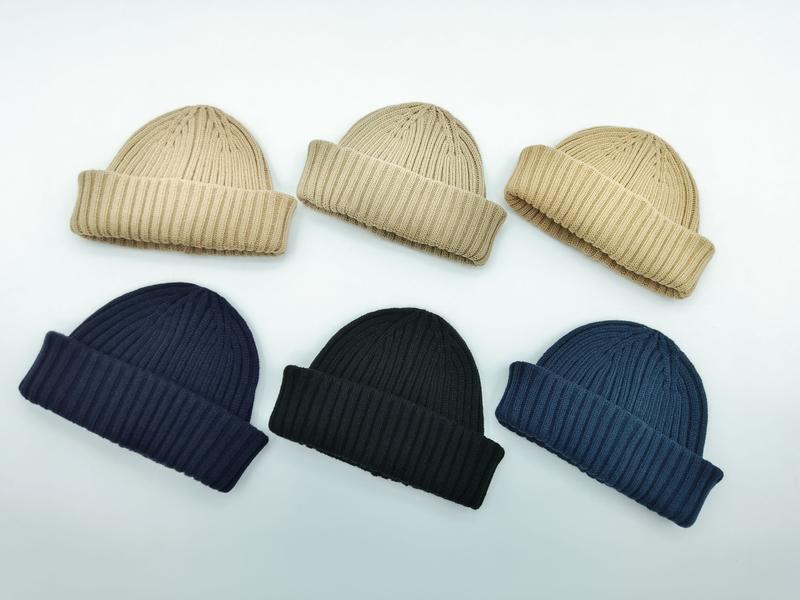 Six ribbed knit folded cuff beanies arranged in two rows in beige, navy, black, and steel blue colorways on white background