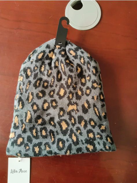 Grey and black leopard animal print knit beanie hat with tan spots, displayed on retail hanger with tag
