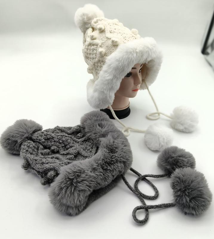 White and gray chunky knit trapper hats with faux fur lining, ear flaps, and pom pom ties displayed on mannequin head