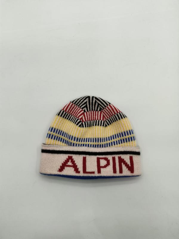 Colorful knit beanie hat with red yellow blue black stripes and ALPIN text on white ribbed cuff, laid flat on white background
