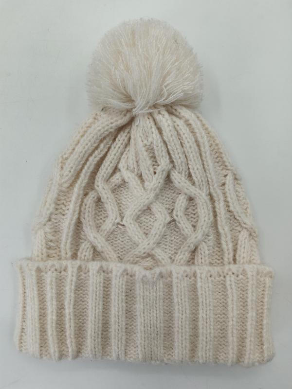 Cream cable knit winter beanie hat with fluffy pom pom on top and ribbed cuff, laid flat on white background