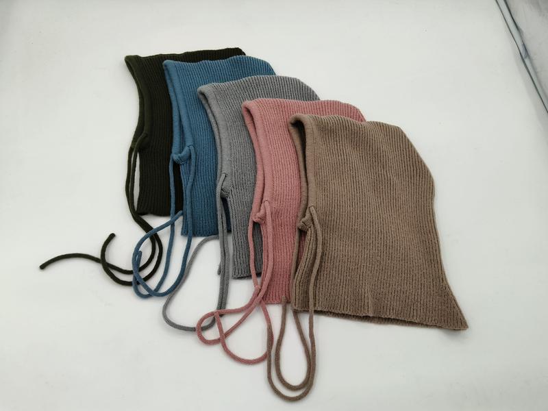 Five ribbed knit baby bonnets with chin tie strings in olive, blue, gray, pink, and taupe laid flat on white background