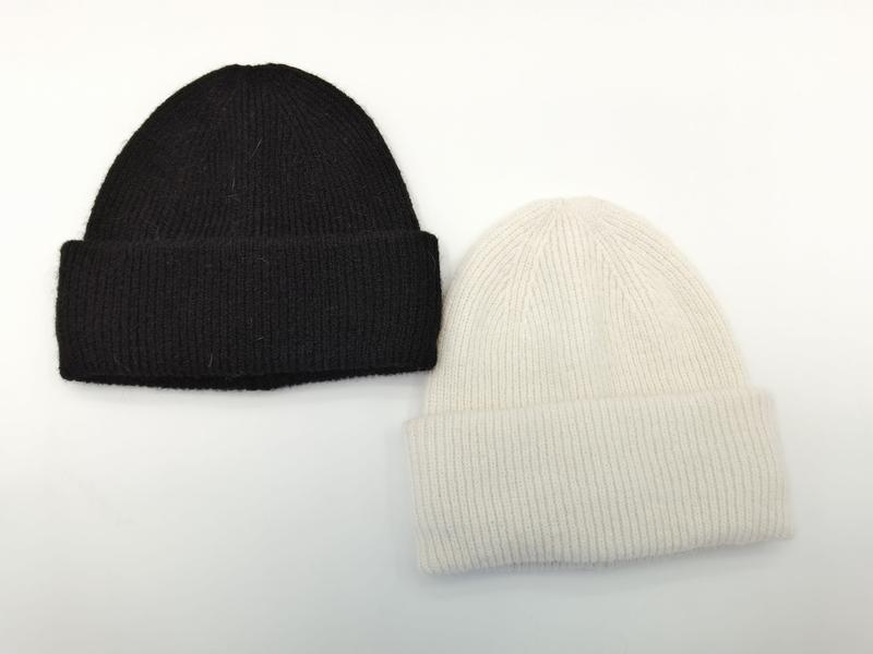 Two ribbed knit cuffed beanie hats laid flat, one black and one cream white, soft wool-blend winter beanies