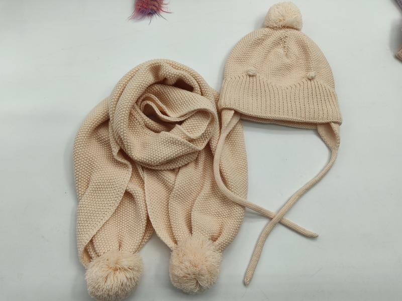 Cream knit children's winter hat with ear flaps and pom pom top paired with matching scarf with pom pom ends