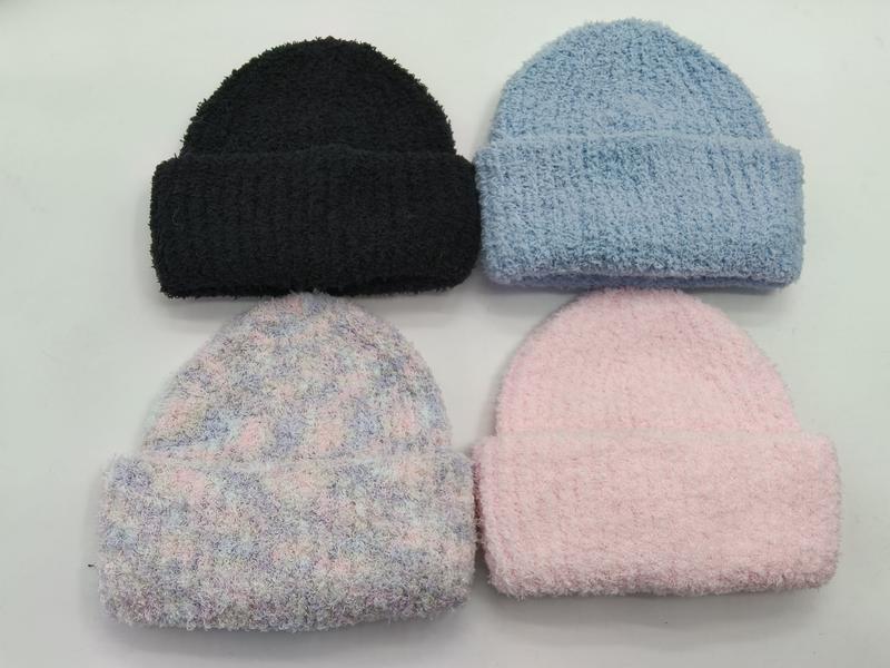 Four fluffy knit beanies laid flat in black, light blue, pastel tie-dye, and soft pink colorways on white background