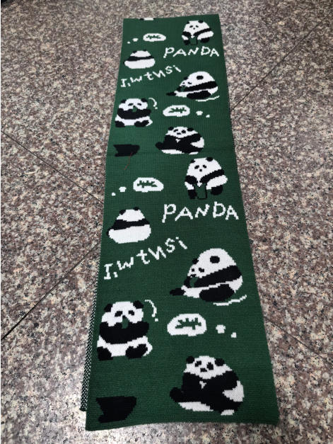 Dark green knitted scarf featuring repeating black and white panda bear illustrations with PANDA text, laid flat on tile floor