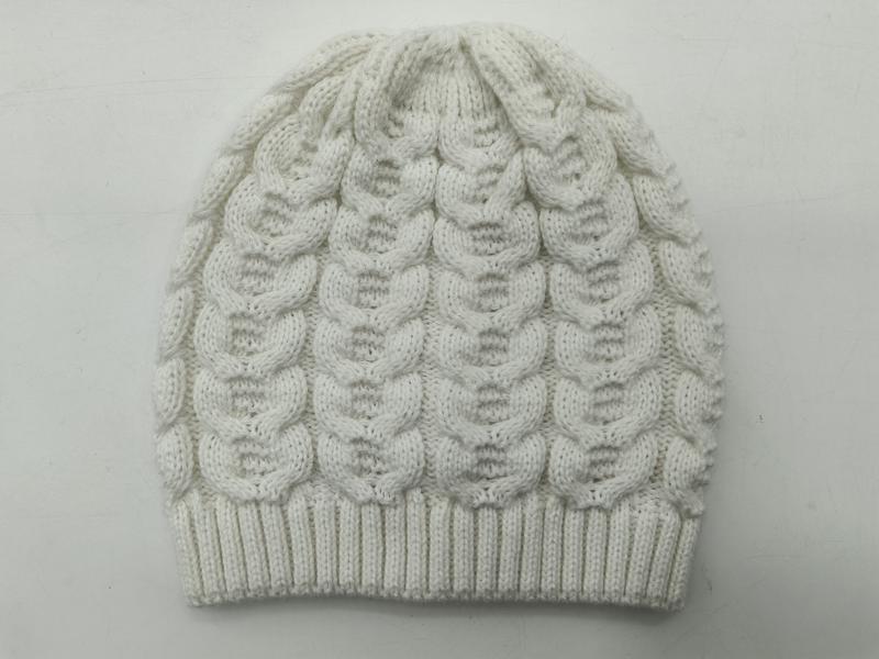 White cable knit winter beanie hat with bubble pattern texture and ribbed cuff, laid flat on light background