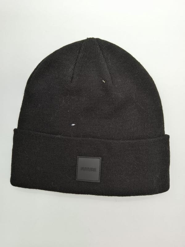 Black ribbed knit beanie hat with folded cuff and square FUTURE rubber patch label on white background