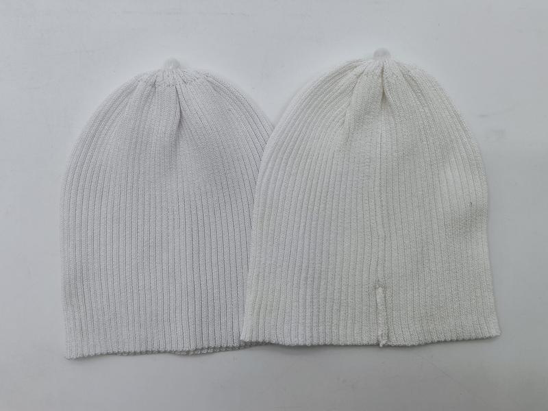 Two ribbed knit beanie hats laid flat, one light gray and one off-white, showing fine rib texture and slouchy fit