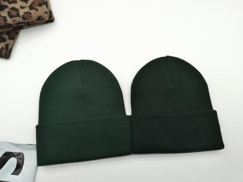 Two dark forest green ribbed knit cuffed beanie hats laid flat on white surface next to leopard print fabric