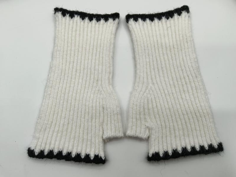 Pair of white ribbed knit fingerless mittens with black zigzag trim at cuff and top, laid flat on white background