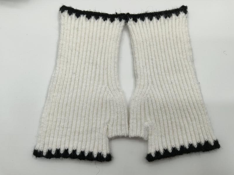 Flat lay of handknitted white ribbed fingerless mittens with black contrast trim at cuffs and wrist openings