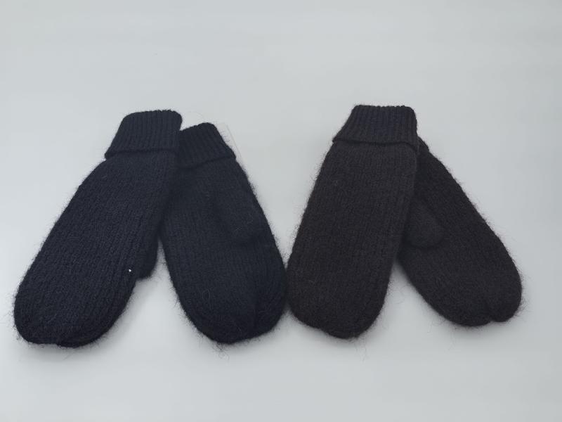 Two pairs of chunky knit mittens in black and dark brown laid flat on white background, showing ribbed cuffs and fluffy texture