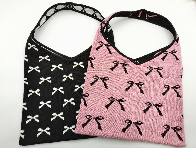 Two knit hobo bags with allover bow pattern, one black with white bows and one pink with black bows, shoulder straps