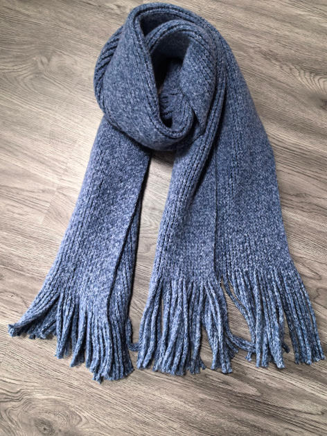 Long chunky knit grey marl winter scarf with tassel fringe ends, folded on wooden floor