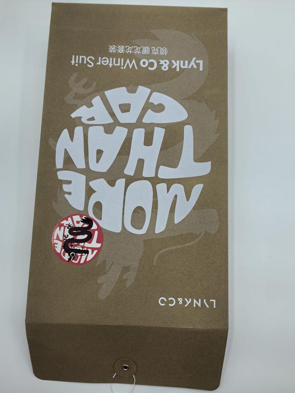 Upside-down kraft brown gift box printed with 'More Than Core' text, dragon sticker, and Lynk & Co Winter Suit branding